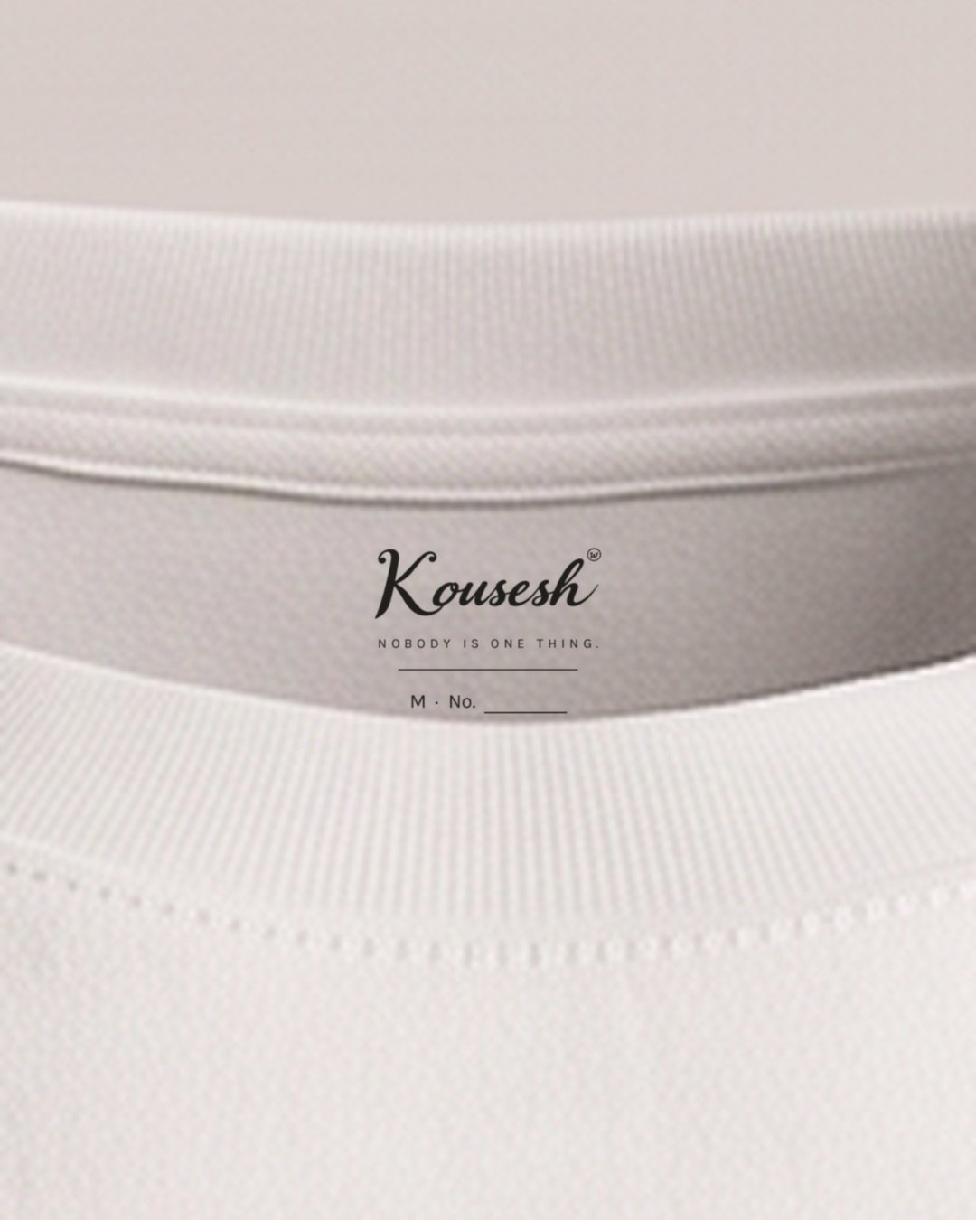 Inside the neckline, a label printed into the cotton reading Kousesh, NOBODY IS ONE THING., and a blank line for the hand-written number