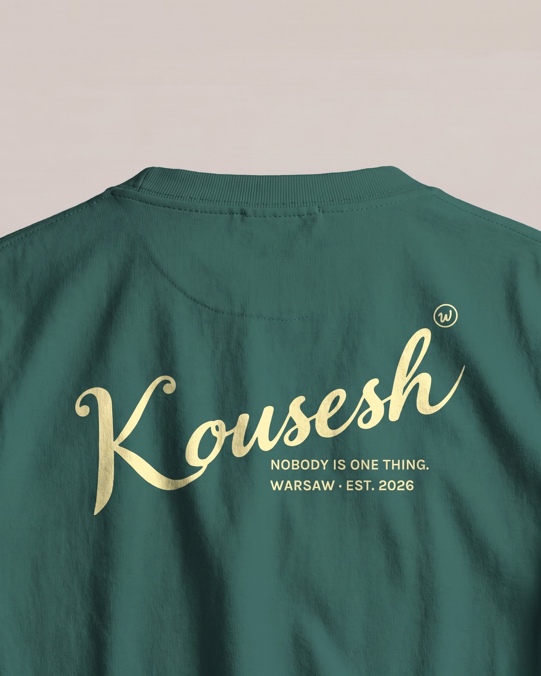 Close-up of the back, Kousesh in pale yellow script with NOBODY IS ONE THING. and WARSAW · EST. 2026 underneath