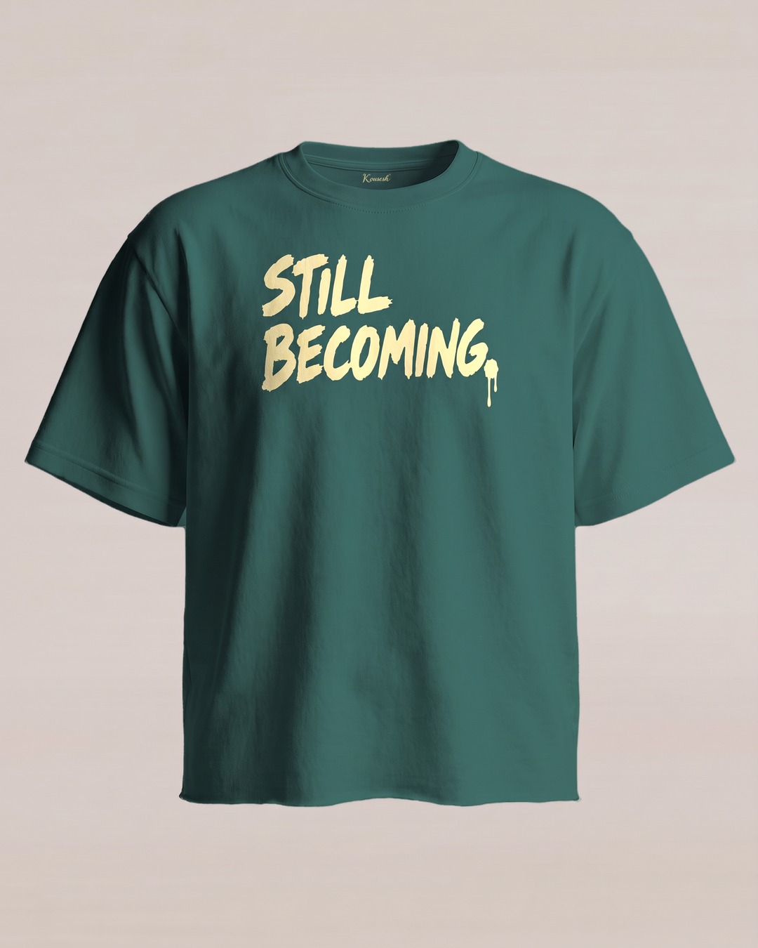 Tee 01, front: a deep green tee with a raw hem, STILL BECOMING. in large pale yellow brush-style letters across the chest