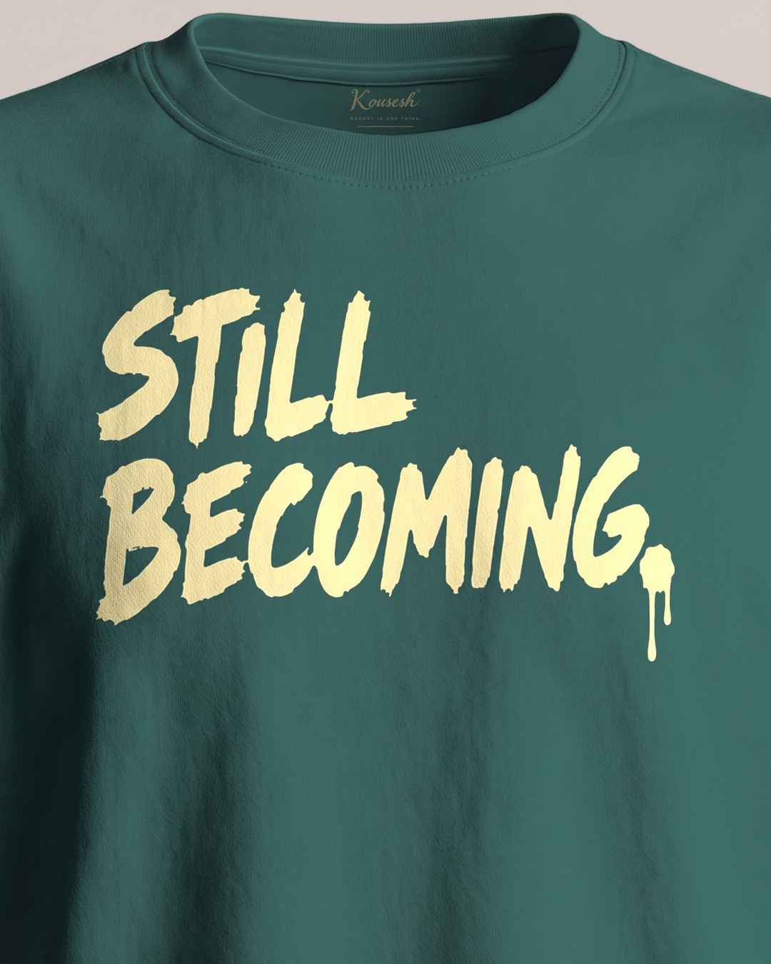Close-up of the front print, STILL BECOMING. in pale yellow with a drip of paint running off the full stop