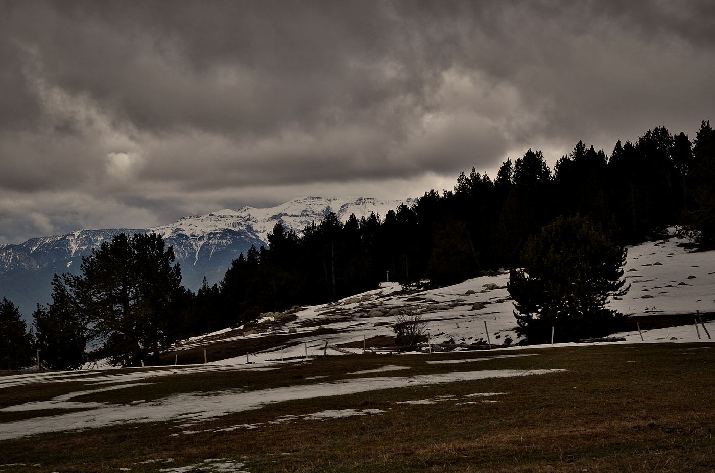 Snow patches and dark pine ridges in the Catalan Pyrenees under heavy cloud